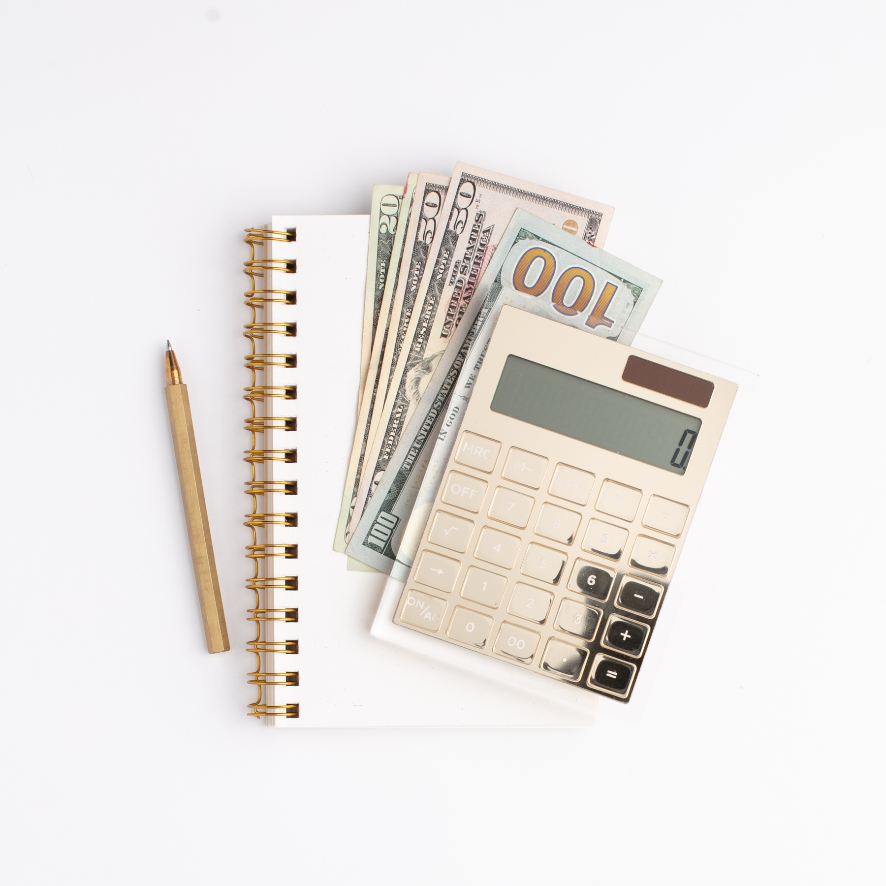 gold calculator on top of a stack of cash and notebook with a pencil on a white background